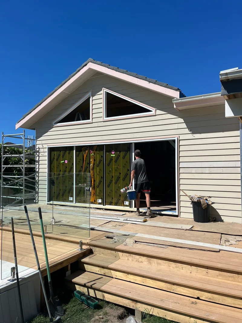The same extension during construction: cladding on, door frames in place, a tradesperson carrying tools through the opening and scaffolding at the side