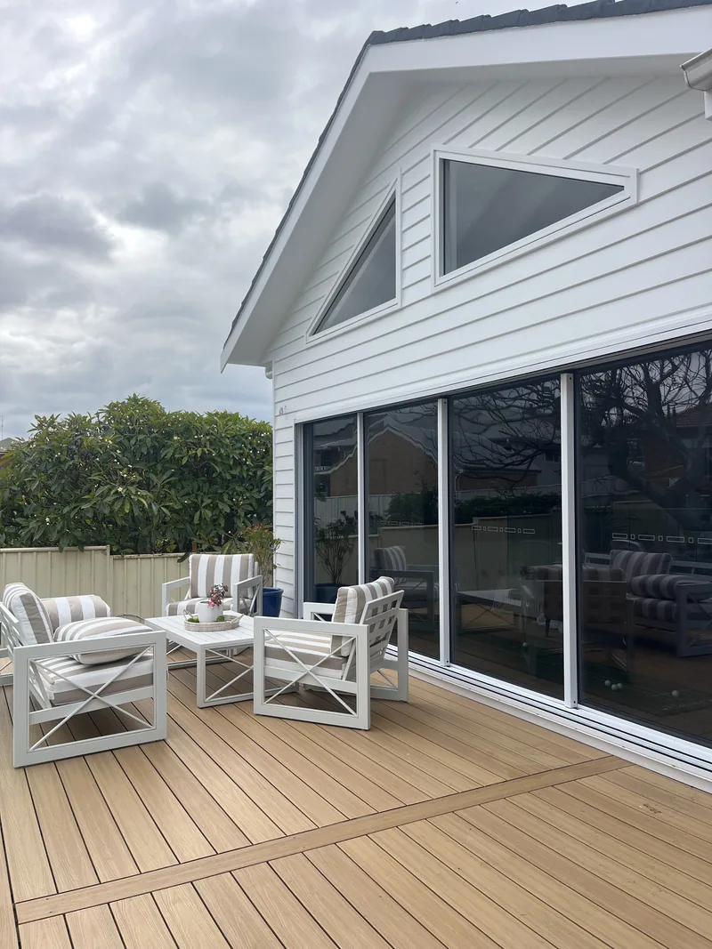 White weatherboard-style extension with triangular gable windows above a wall of sliding glass doors, beside a timber deck