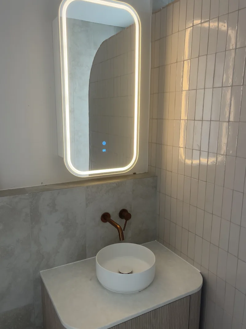 Bathroom with a floating fluted vanity, a round vessel basin, brass wall tapware and a backlit mirror