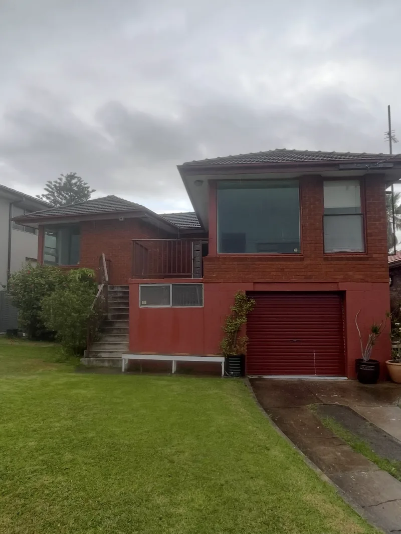 The house before the renovation: red brick, with a red roller garage door, a small balcony and concrete stairs up from the lawn