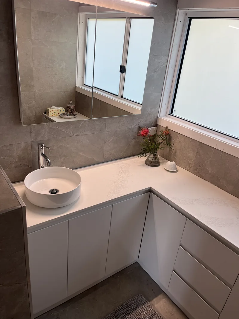 Corner vanity with a round vessel basin, a white benchtop and large grey wall tiles