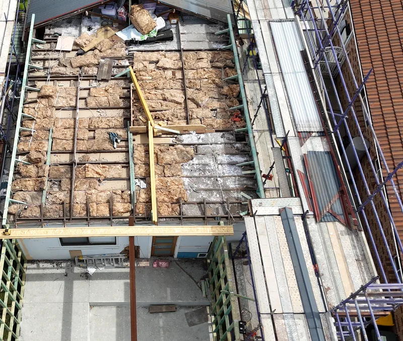 Aerial view of a house with the back section of its roof removed, exposing the ceiling joists, with scaffolding along both sides