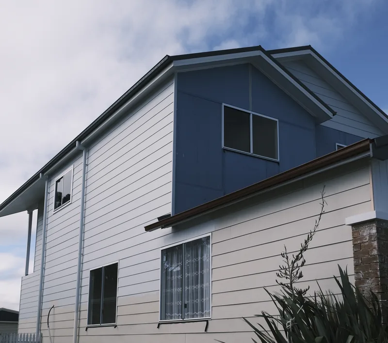 Side view of a two-storey house with weatherboard cladding on both levels and the front gable still in blue sheeting